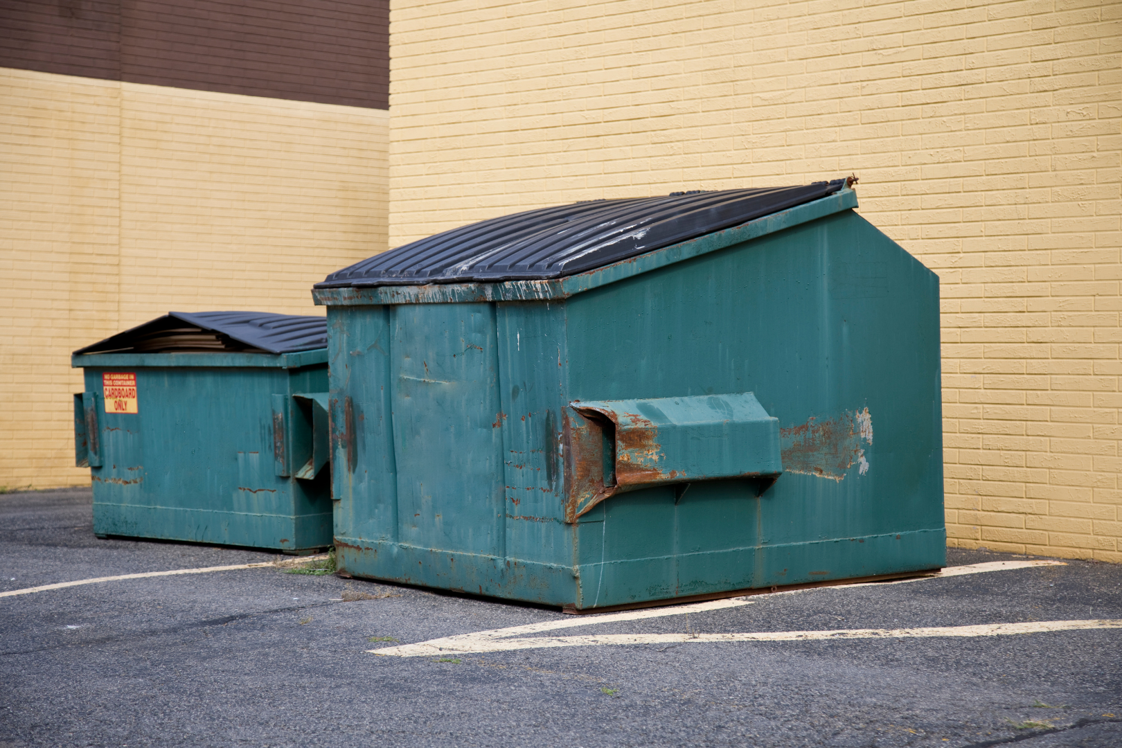 Two teal dumpsters beside a brick wall on an empty parking lot