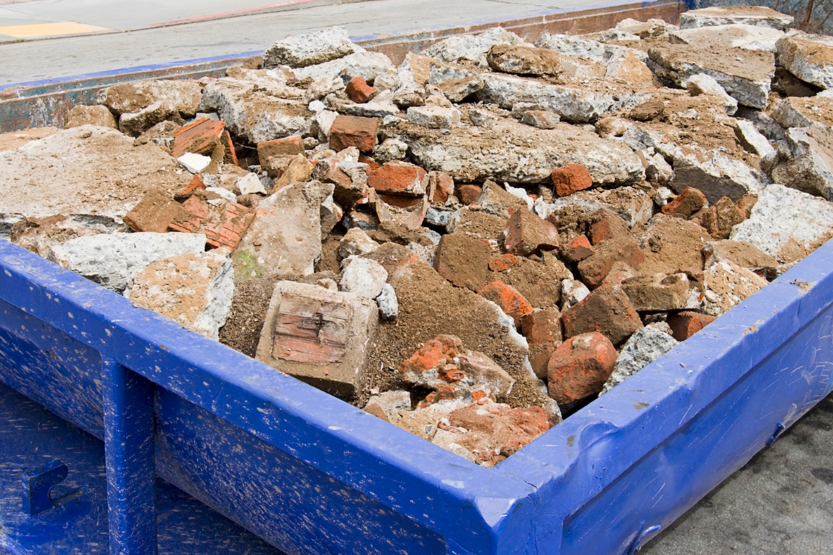 Blue dumpster filled with broken bricks, concrete, and rubble from demolition