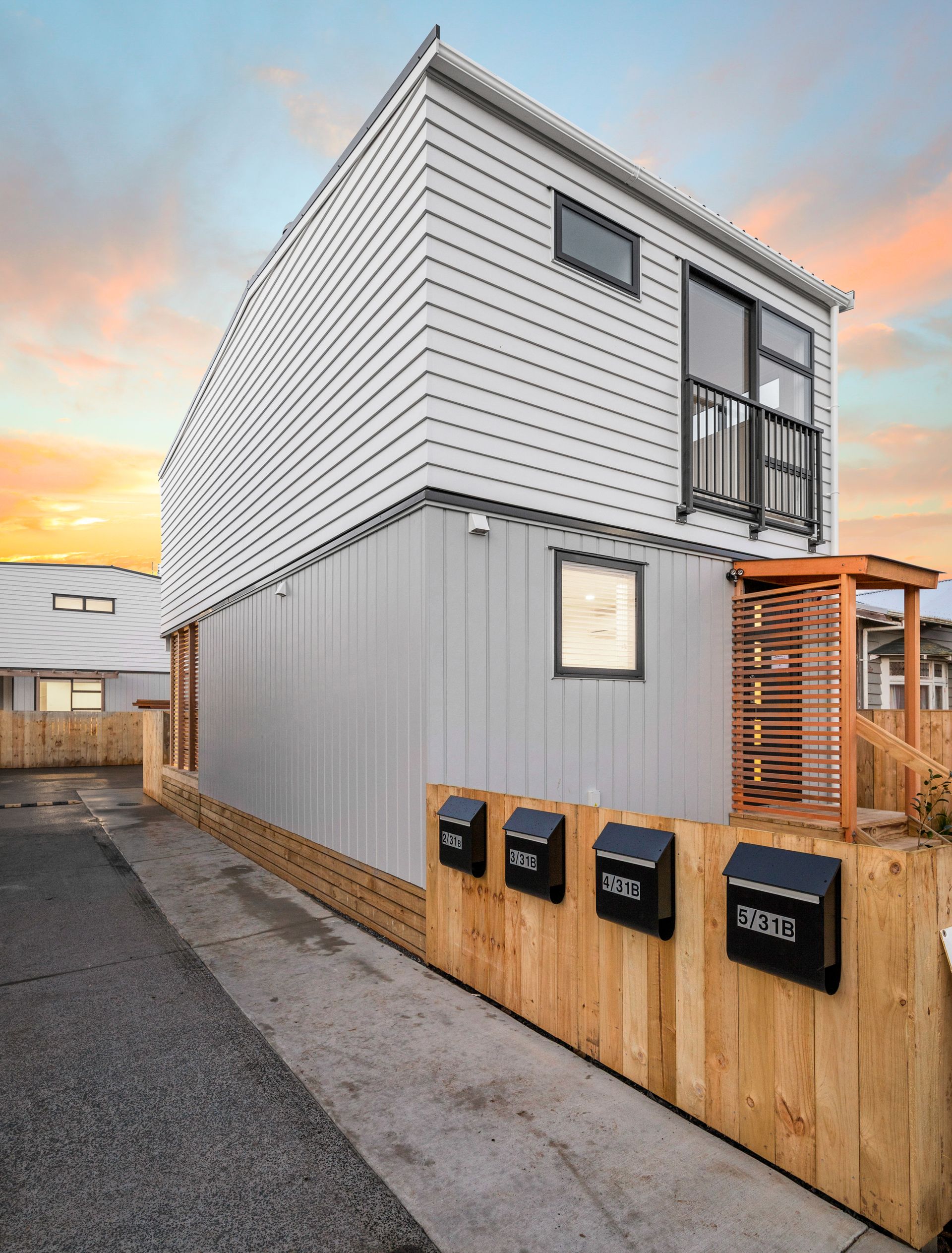 Modern multi-unit dwelling with light gray siding, a wooden fence, and black mailboxes.