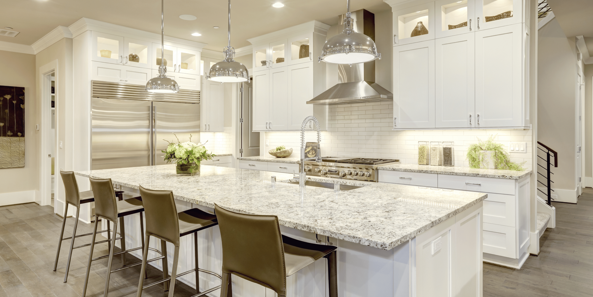 A bright white kitchen with granite island, stainless steel appliances, and light-colored bar stools.