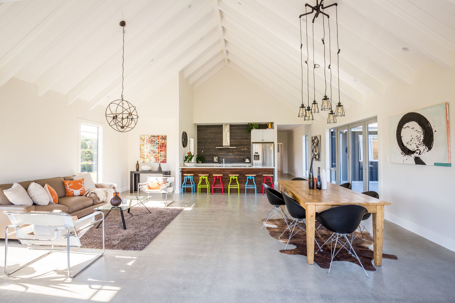 Open-plan living area with high ceilings, including a kitchen, dining, and seating area; neutral tones with pops of color.