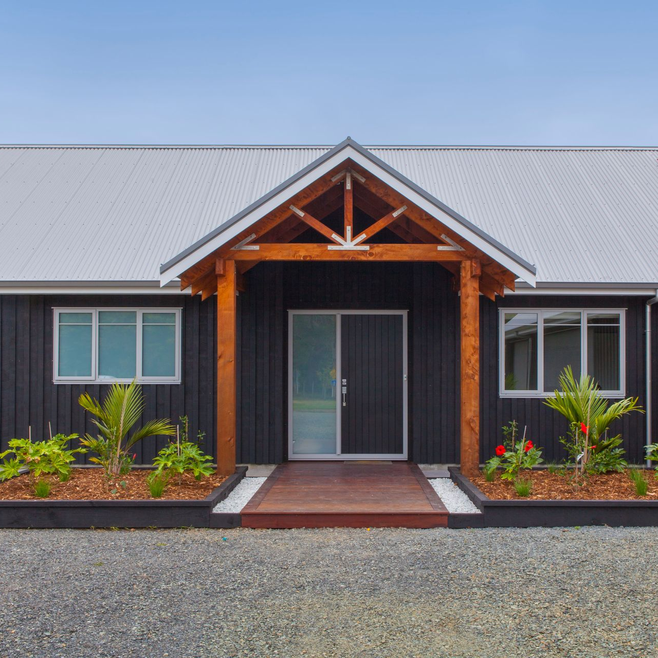 Black house with brown porch, gray roof, and gravel driveway.