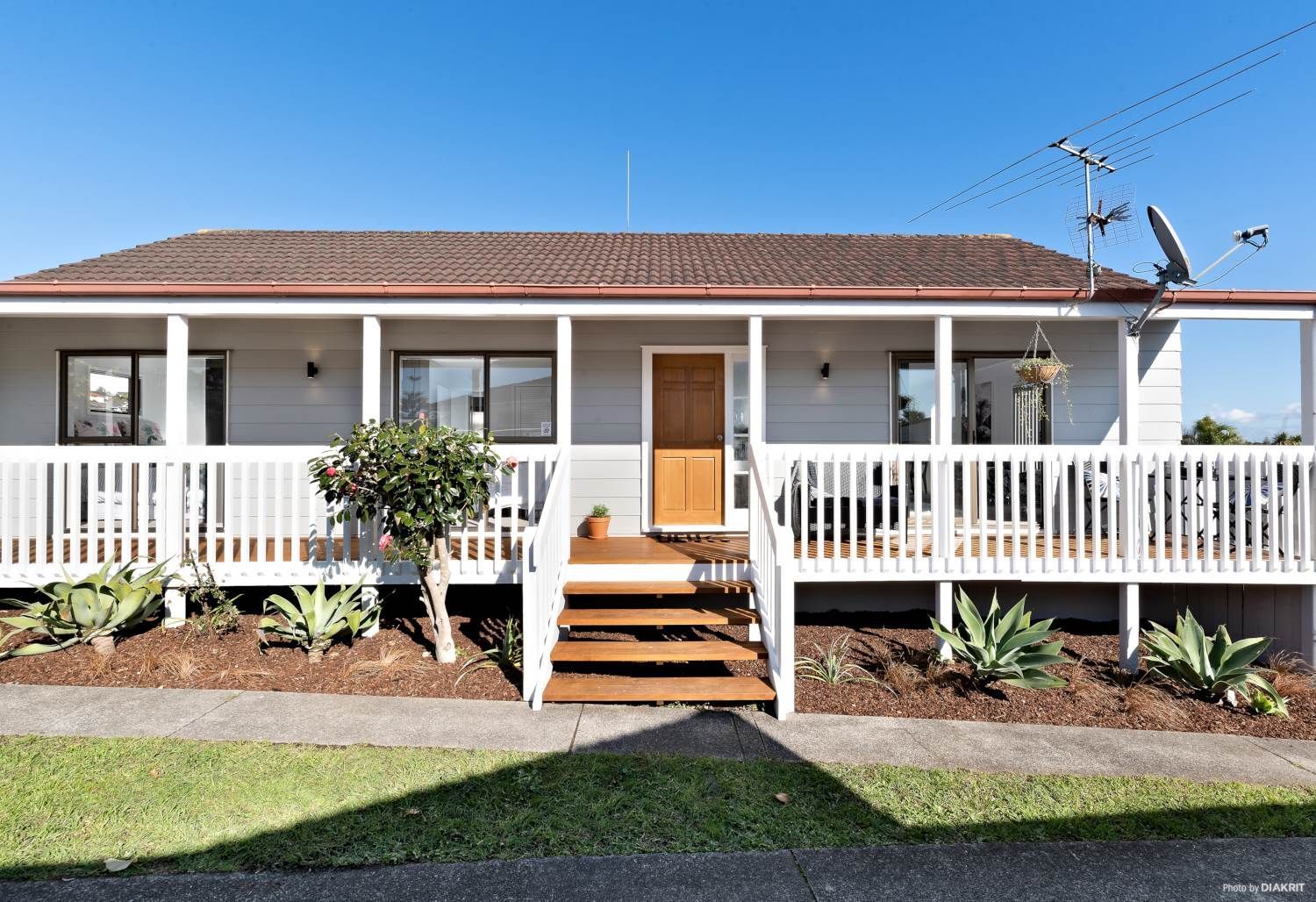 Light blue house with a white porch and brown roof. A brown door leads to the house.