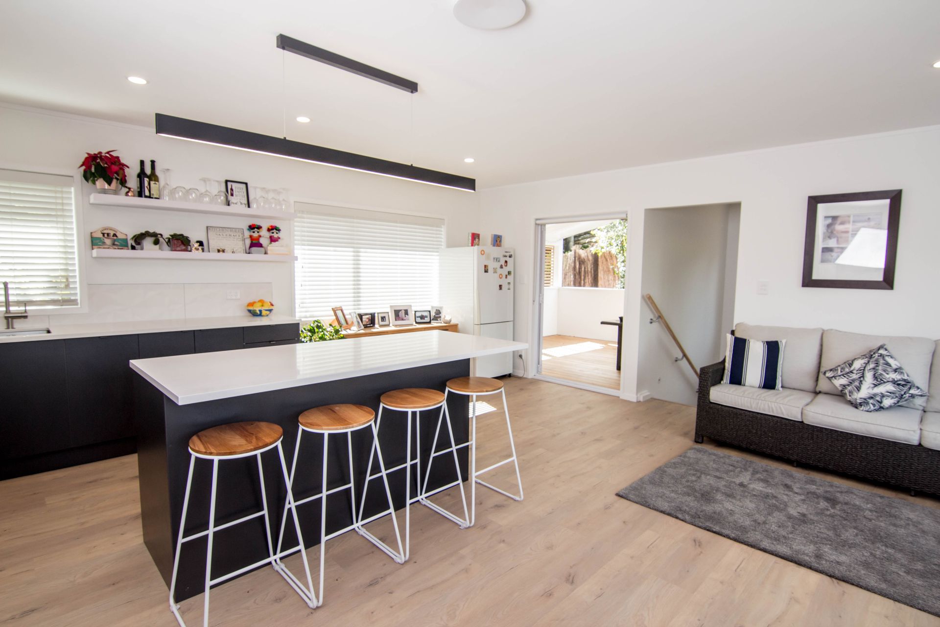 Modern kitchen with black island, white countertops, wood stools, and a living room with a sofa.