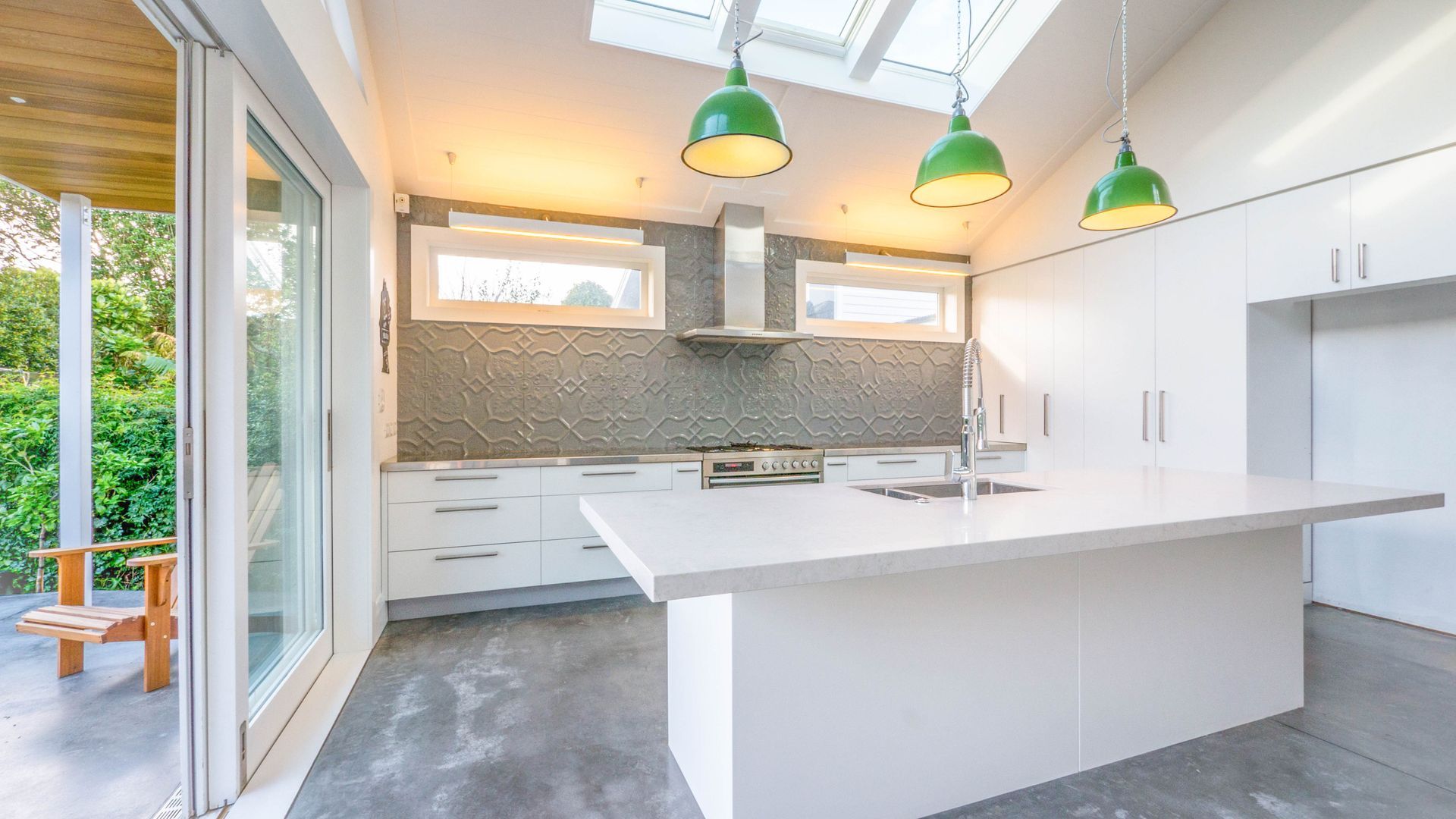 Modern white kitchen with an island, green pendant lights, and sliding glass doors.