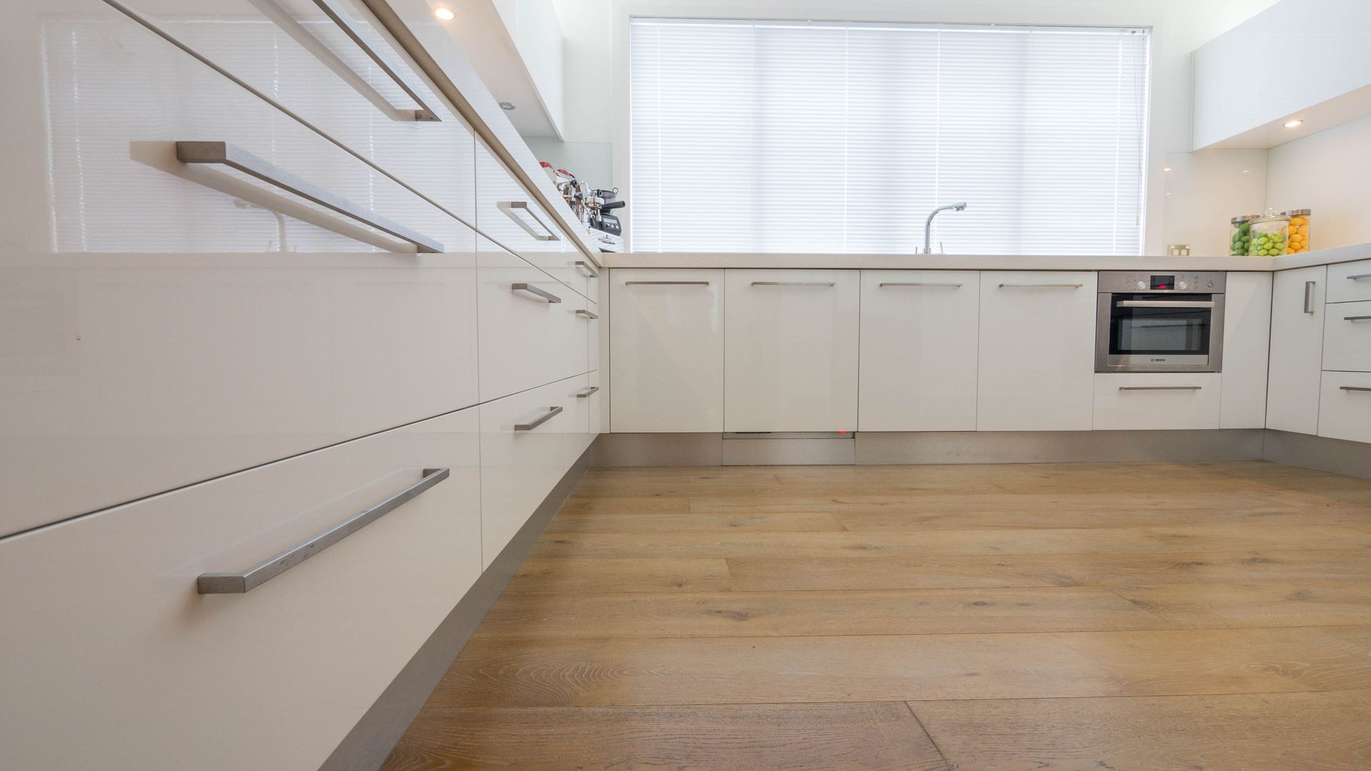 Modern white kitchen with wooden floor; stainless steel appliances and hardware.