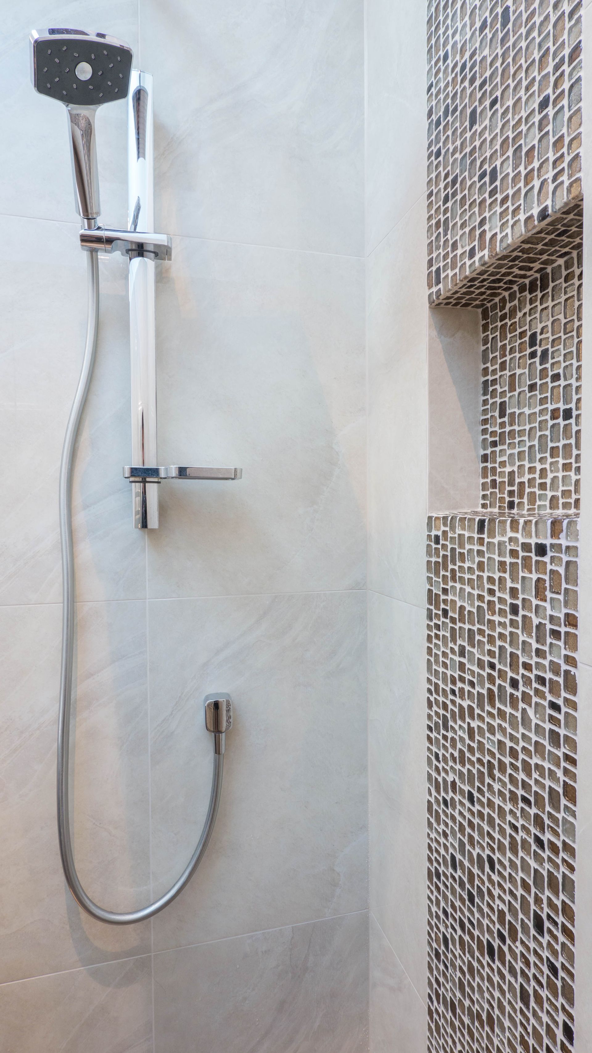 Shower with adjustable chrome showerhead and built-in mosaic tile shelf.