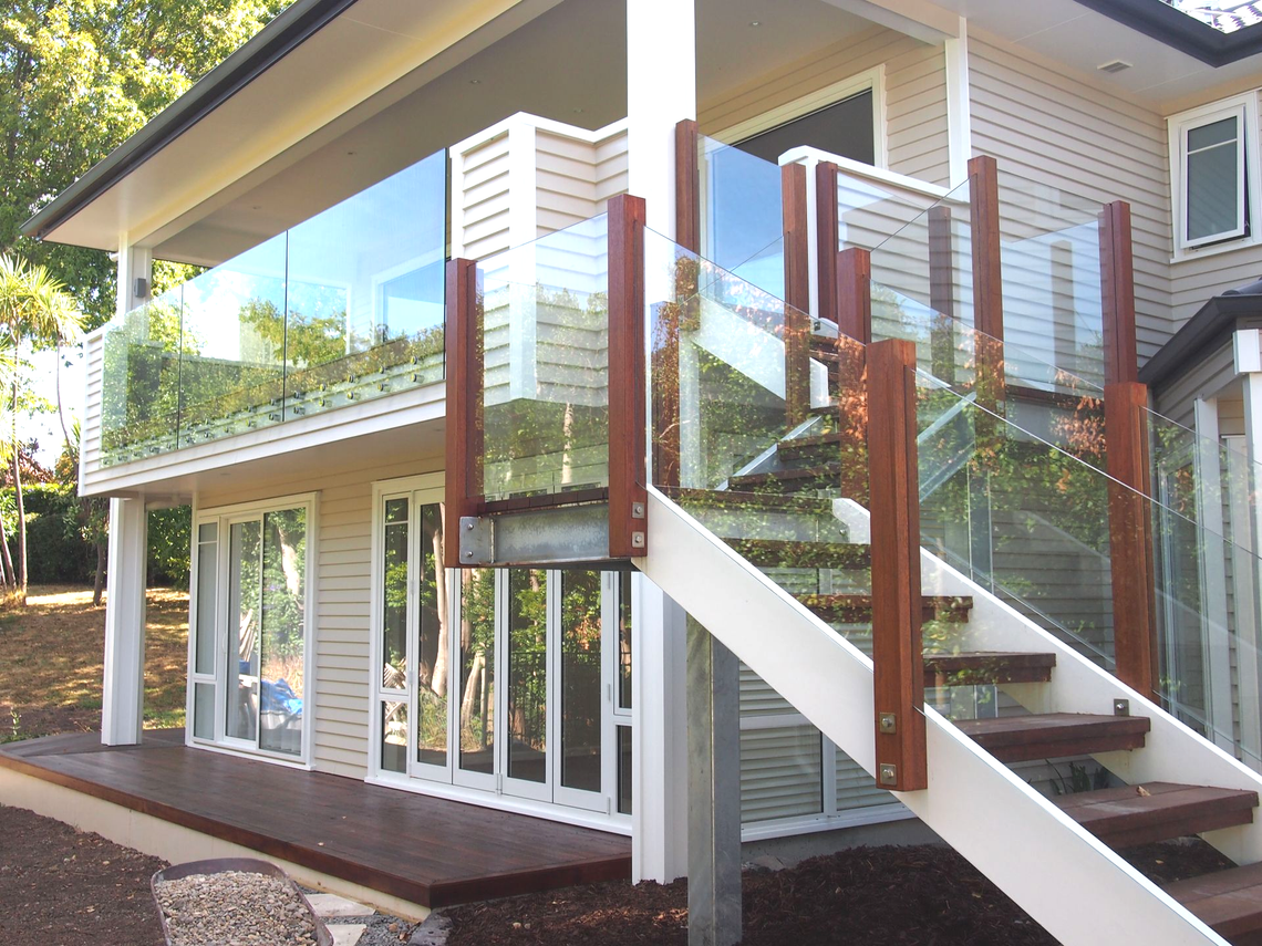 Two-story house with glass railings. Wooden stairs lead to a deck and balcony.