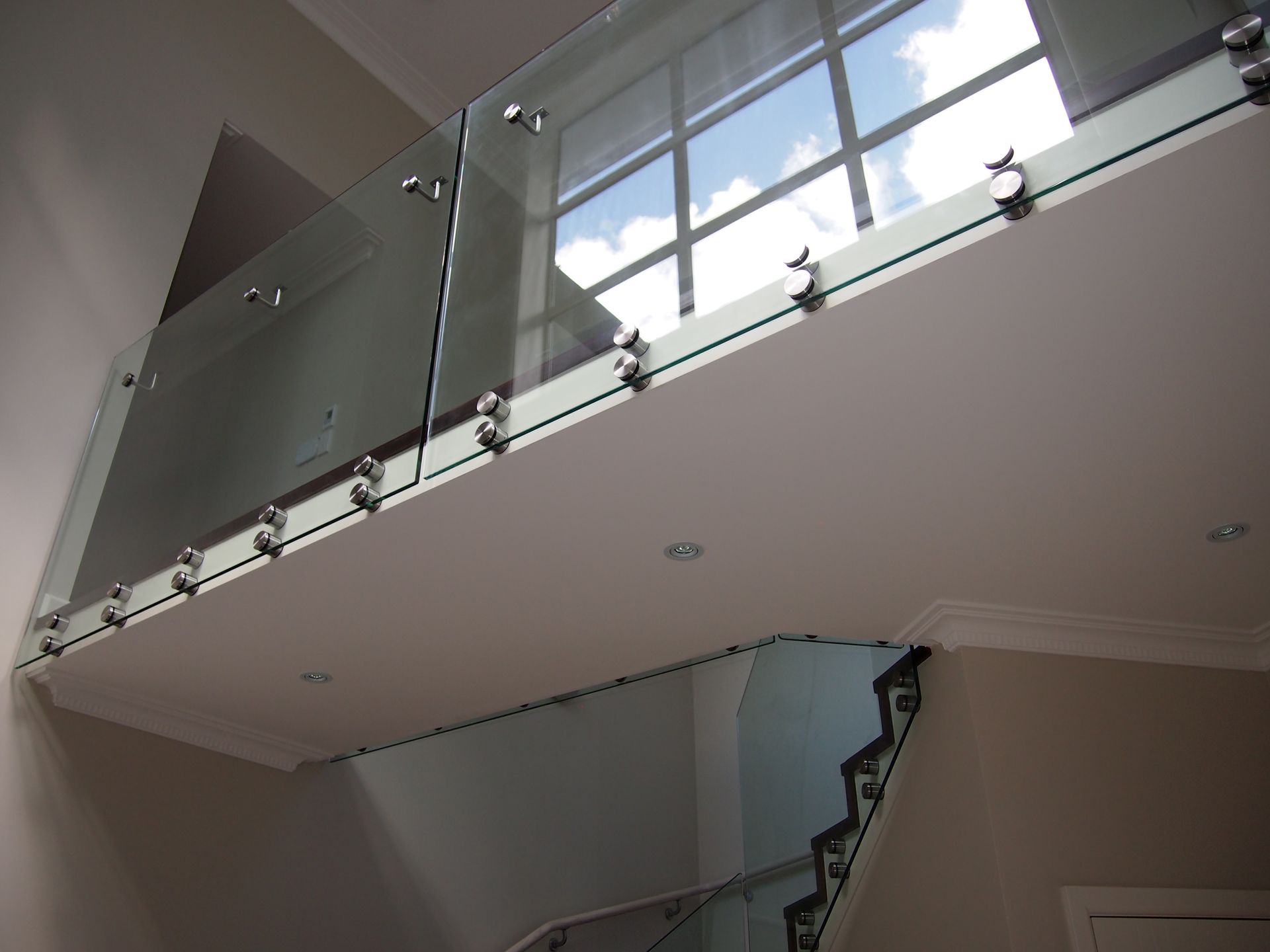 Glass balcony with stainless steel hardware, overlooking a staircase and window.