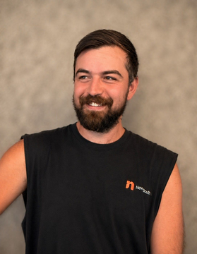 Smiling bearded man in a black sleeveless shirt against a neutral studio backdrop. Rynard