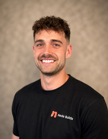 Smiling man in a black shirt against a beige studio backdrop. Sam