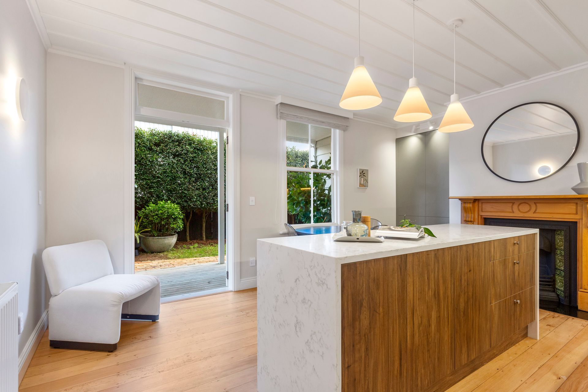 Bright kitchen with wooden island, pendant lights, and a door opening to a garden.