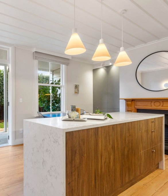 Modern kitchen island with a white stone countertop and wood base, illuminated by three pendant lights.