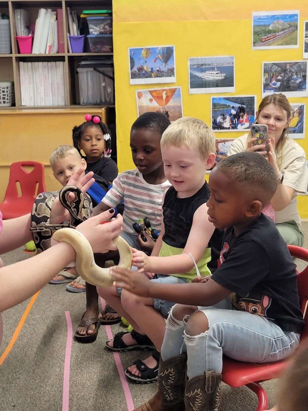 Children coloring green shapes on paper at a wooden table, with crayons and a water cup nearby.