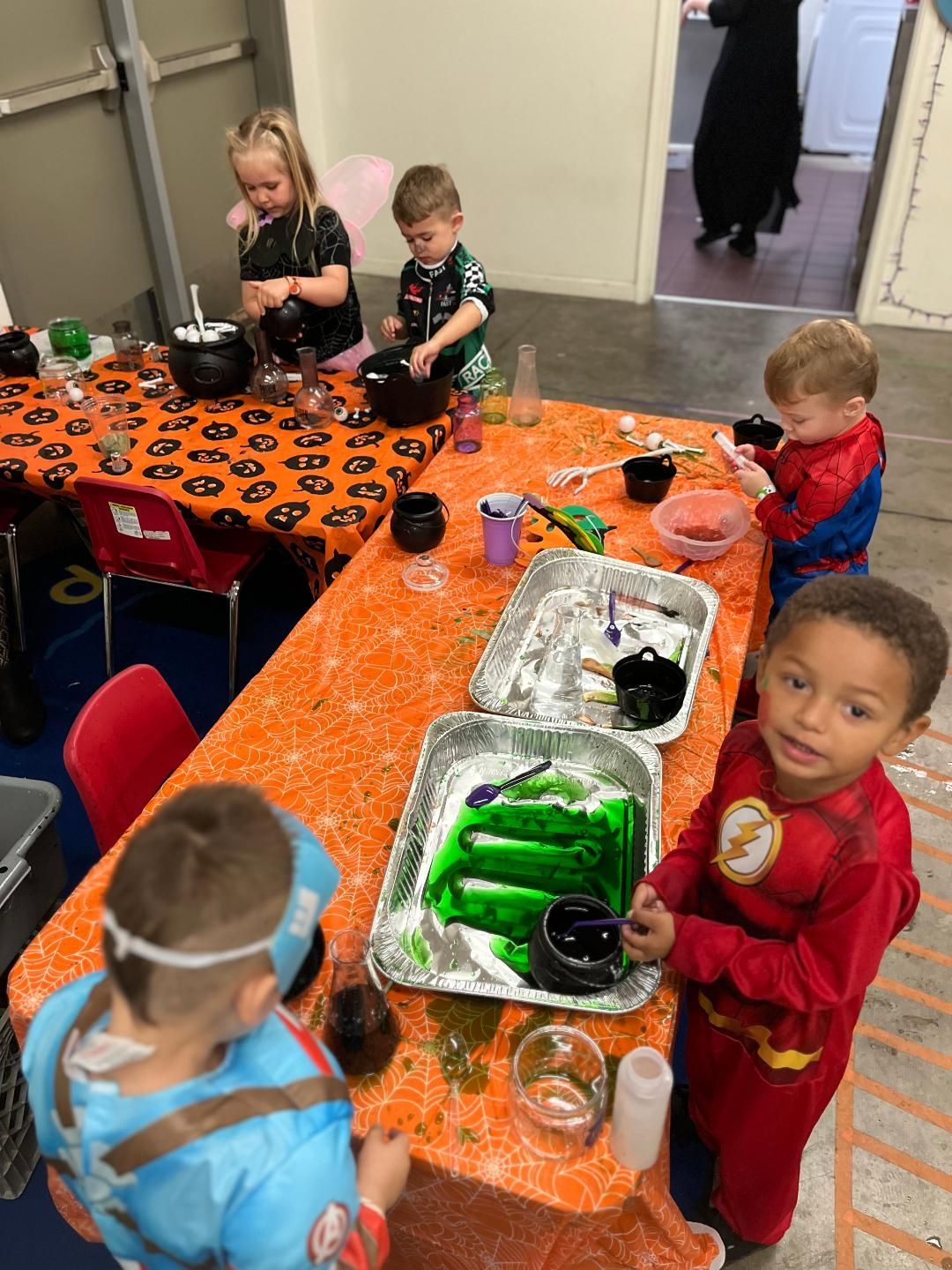 Children in costumes do science activities at a table with Halloween decorations.