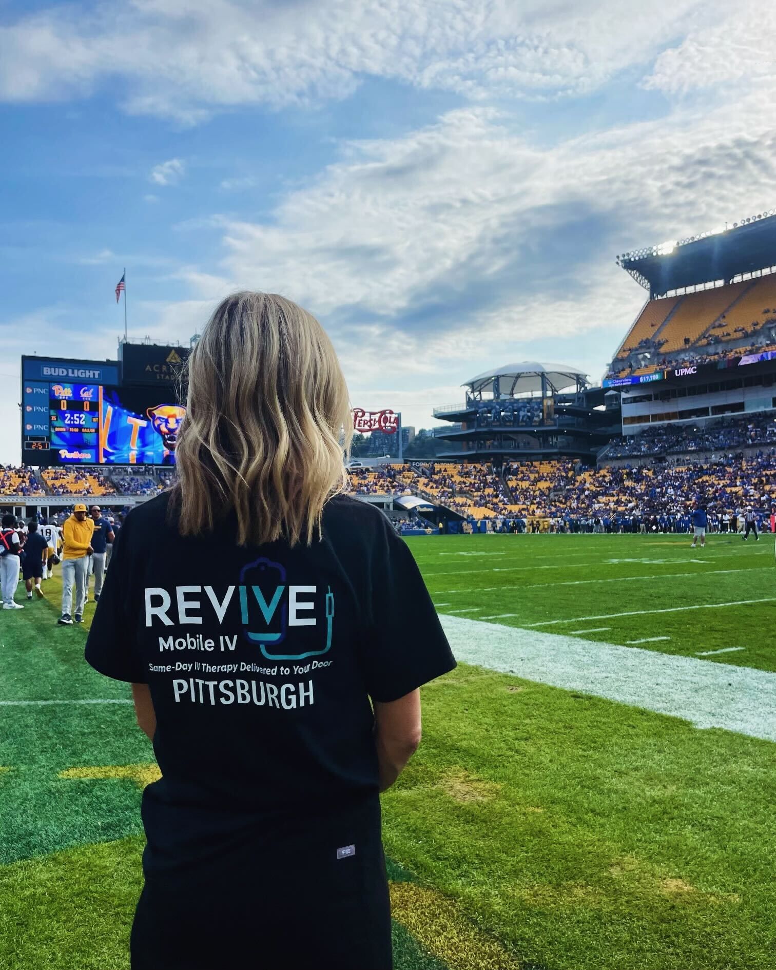 A woman wearing a black shirt that says revive is standing on a football field.