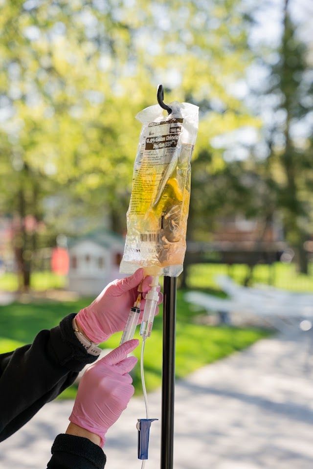 A person wearing pink gloves is holding a bag of IV liquid.
