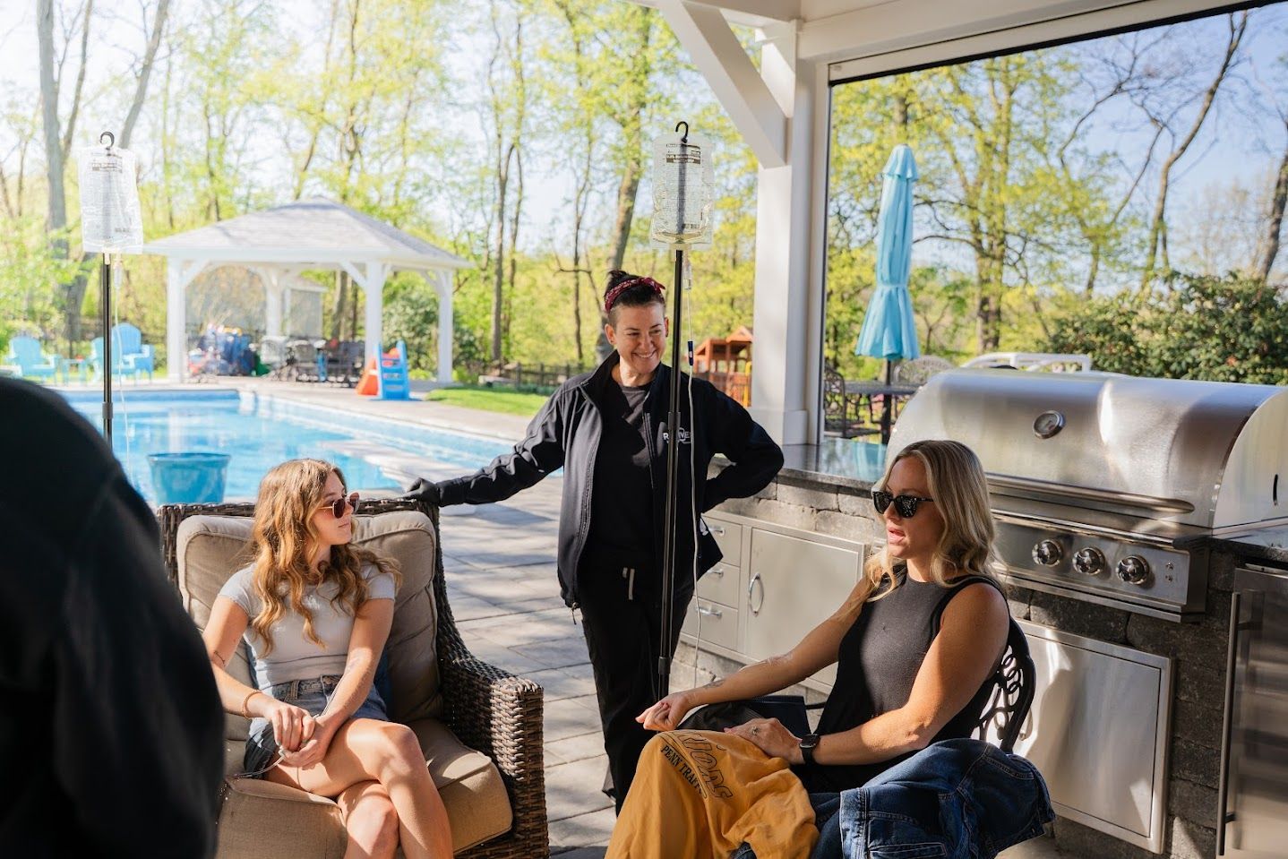 A group of women are sitting on a patio next to a pool with IV drip.