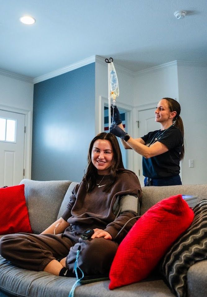 A woman is sitting on a couch with an IV drip.