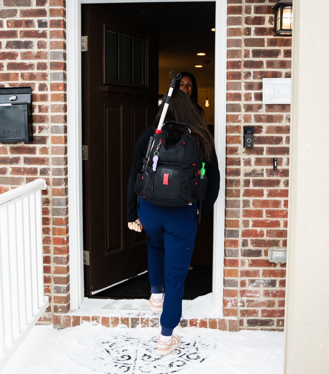 A woman with a backpack is walking into a brick house.