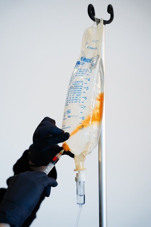 A person is holding a syringe next to a bag of liquid.