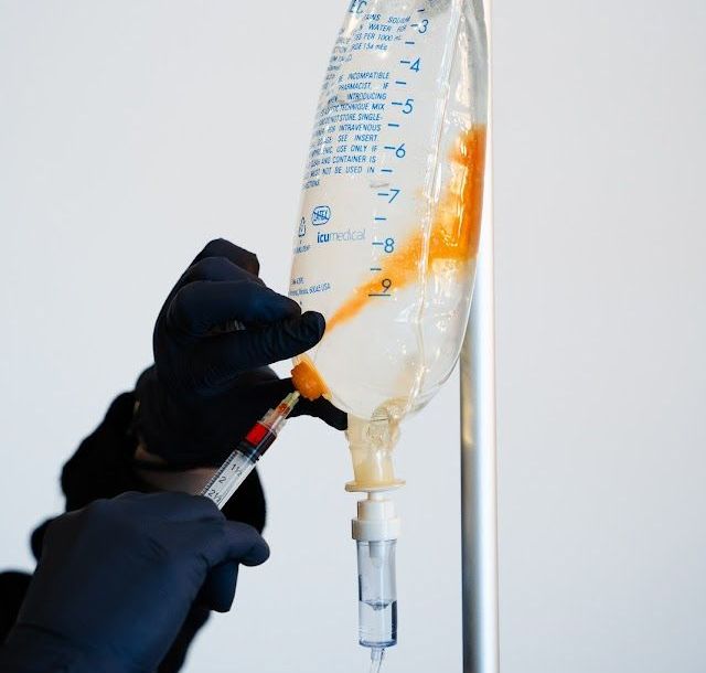 A person is holding a syringe next to a bag of liquid.