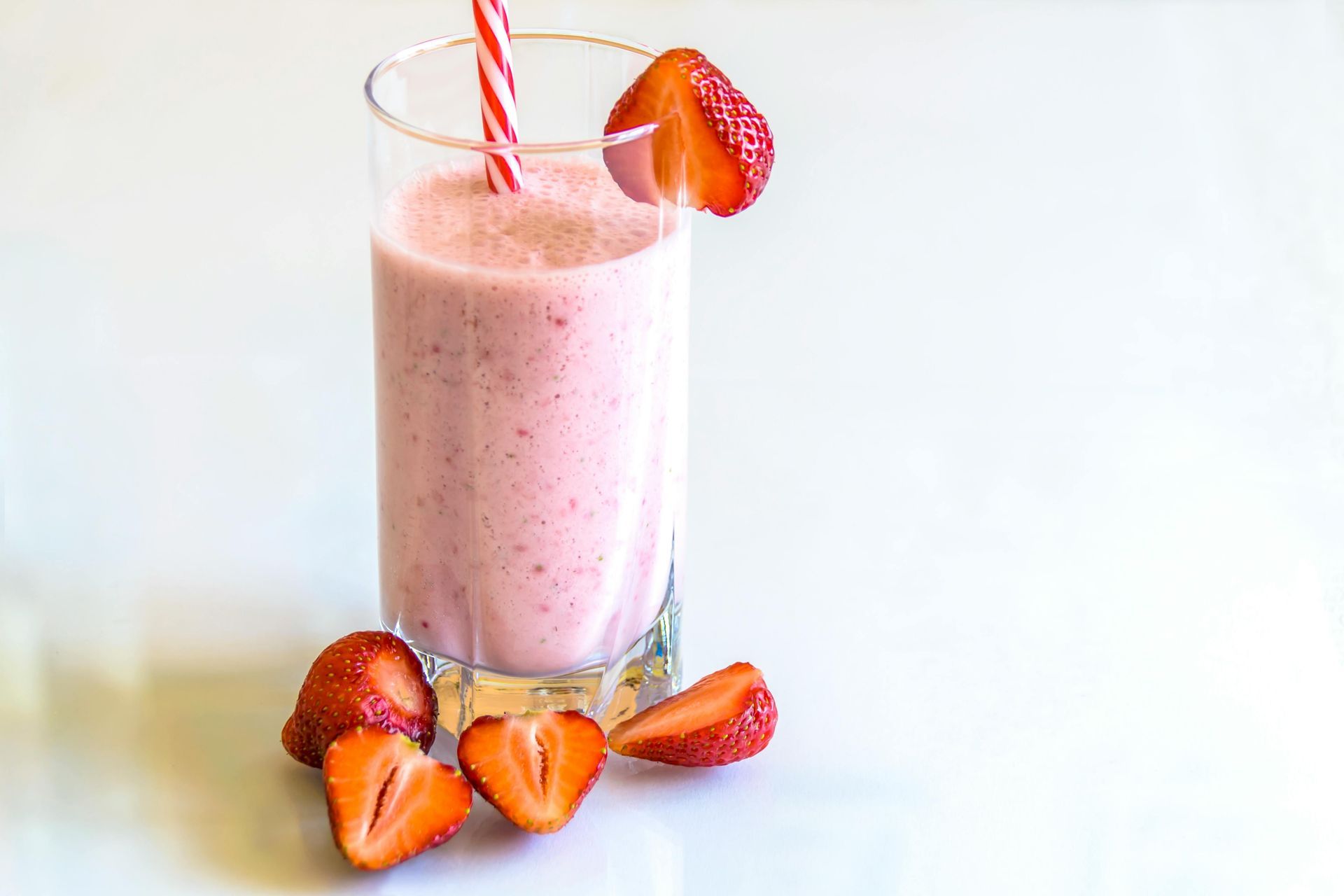 Strawberry smoothie in a glass with a straw, garnished with strawberry slices on a white surface.