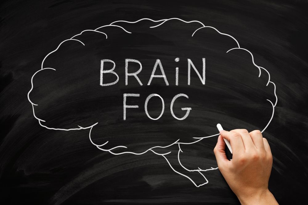 A person is writing the word brain fog on a blackboard