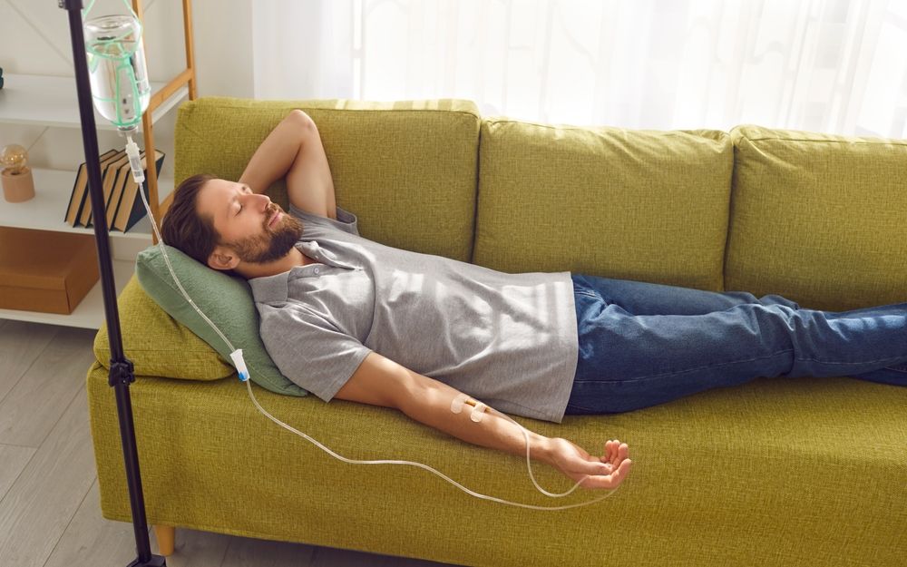 A man is laying on a couch with an iv in his arm.