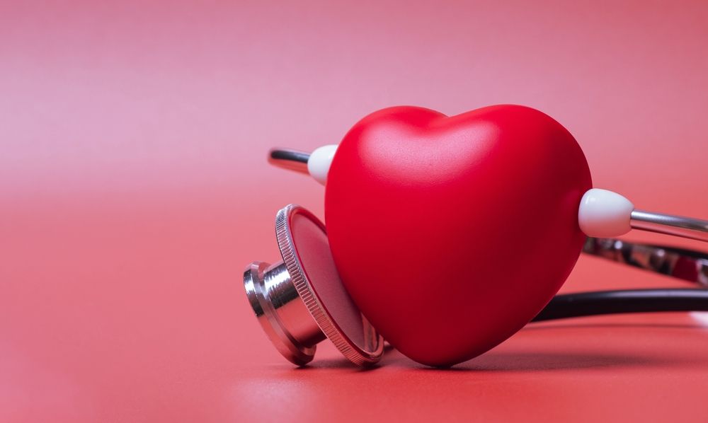 A red heart is sitting next to a stethoscope on a red background.