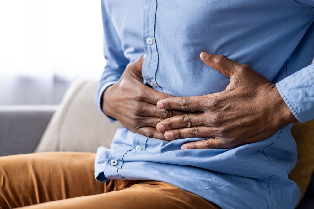 A man is sitting on a couch holding his stomach in pain.