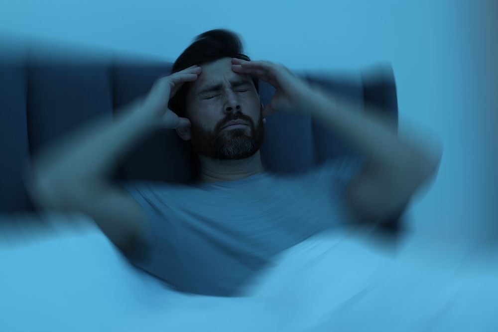 A man is laying in bed with his hands on his head.