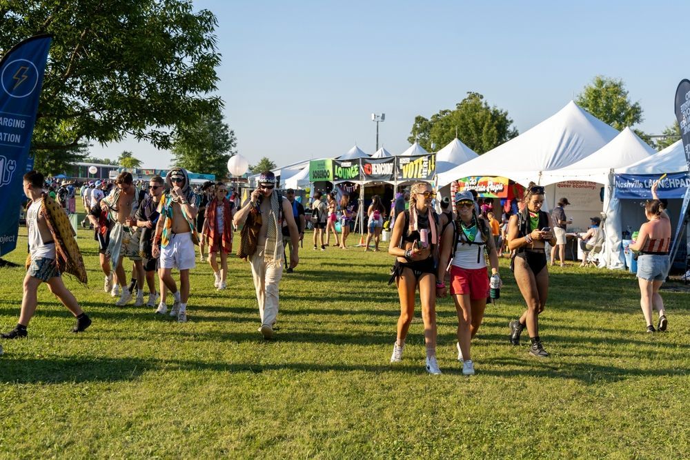 A group of people are walking through a grassy field at a festival.