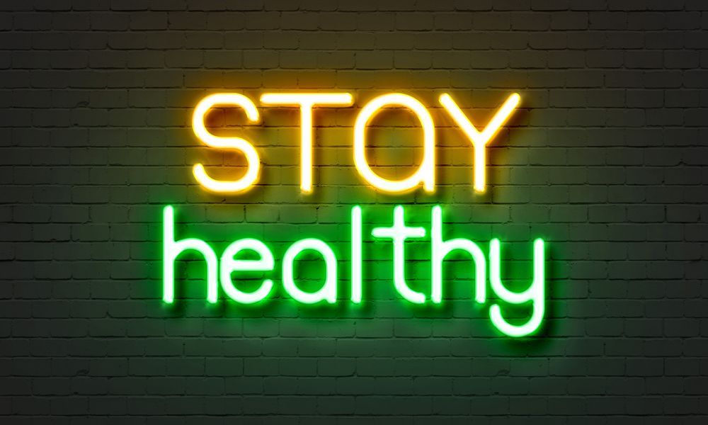 A neon sign that says `` stay healthy '' on a brick wall.