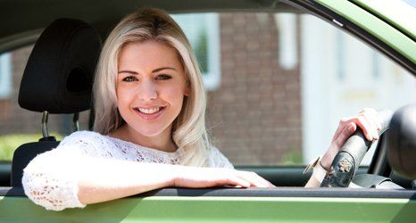 Woman happy in small green car on a sunny day.