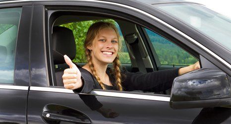 Young woman smiling in car with thumb up.