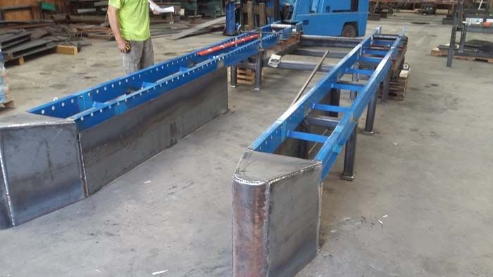 Two long, blue-painted steel framework structures sit on a concrete shop floor, with a person standing nearby.