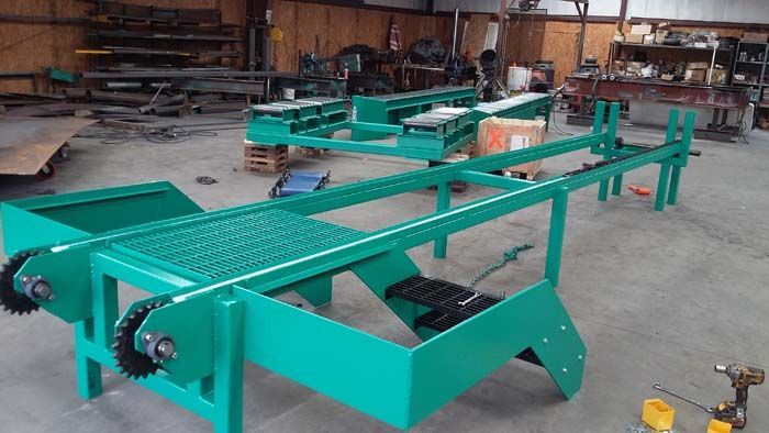 A turquoise industrial conveyor system frame sits on a concrete shop floor with another matching unit in the background.