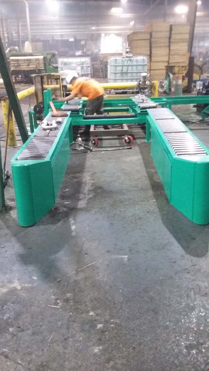 A person in an orange shirt works on a large green industrial conveyor system inside a factory.