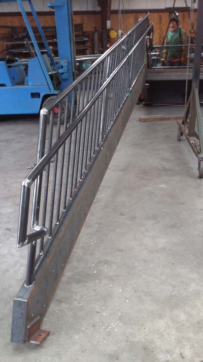 A metal railing with vertical bars mounted to a heavy steel base sits in a workshop near a blue forklift.