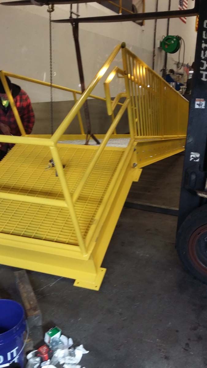 A bright yellow industrial platform with safety railings, being moved in a workshop by a forklift.