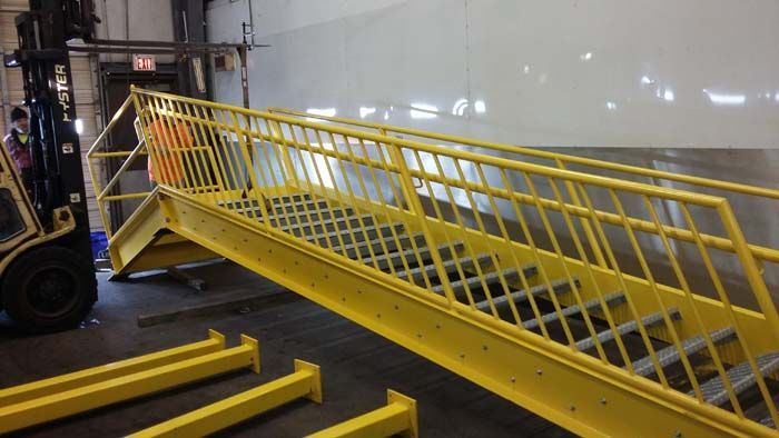 A forklift moves a large, bright yellow industrial metal staircase in a warehouse setting.