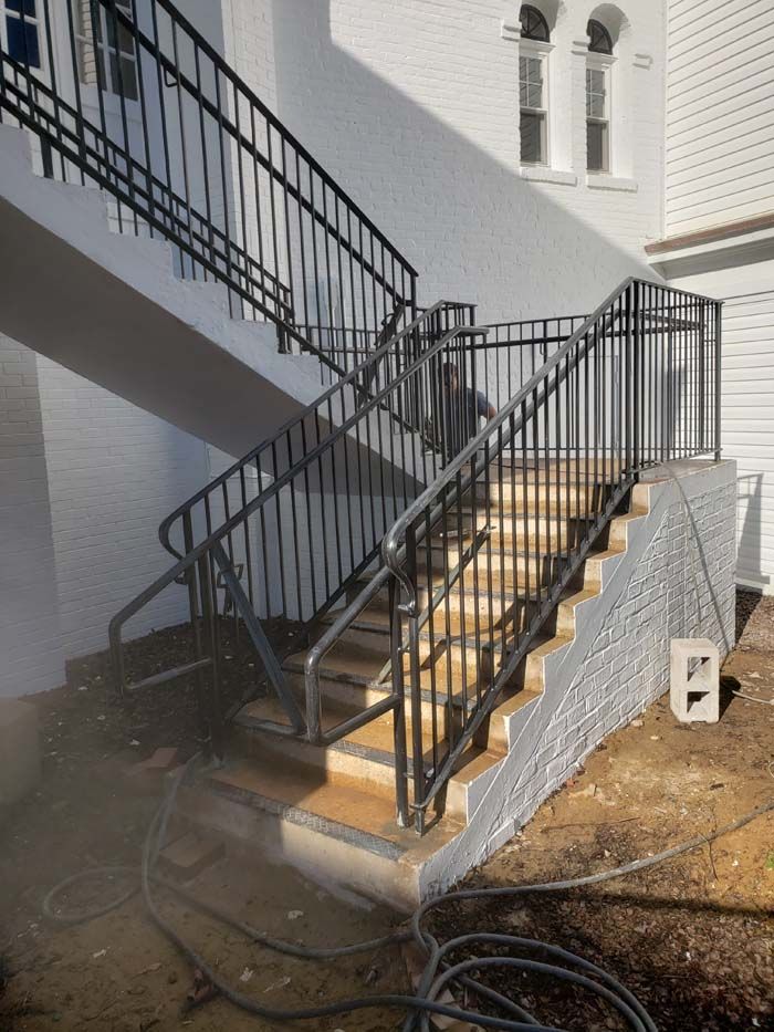 Outdoor concrete stairs with black metal handrails leading up to a white building exterior.