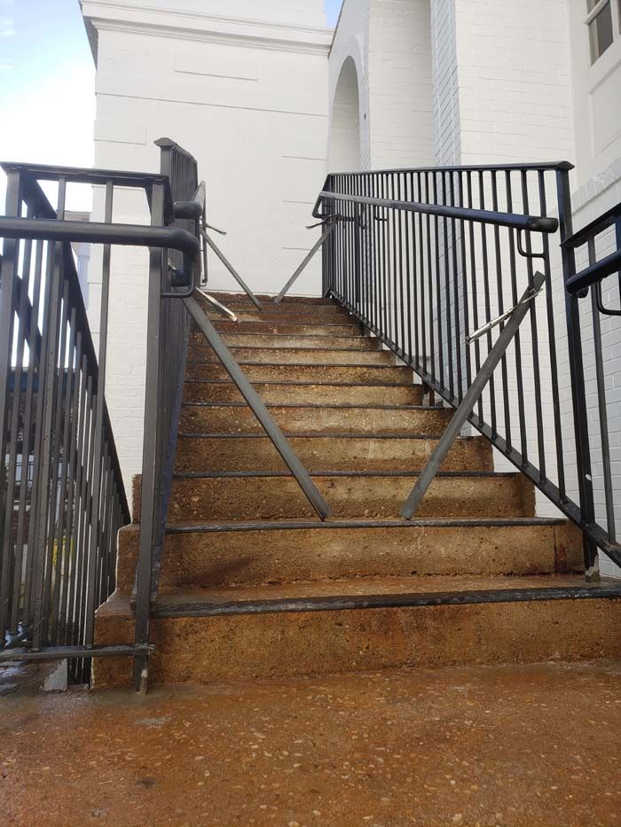 A stone outdoor staircase with a black metal railing that is broken, with its diagonal support bars disconnected.