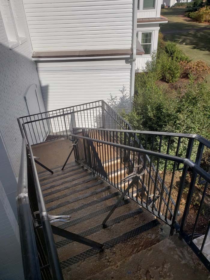 Outdoor metal staircase with black handrails leading down along the white siding of a building.