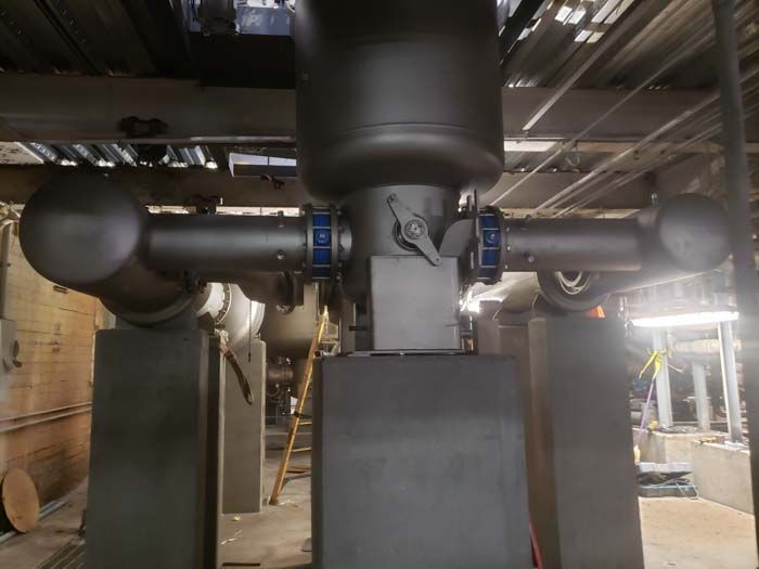 Black industrial pipe system with a central tank, valves, and blue circular connectors inside a facility.