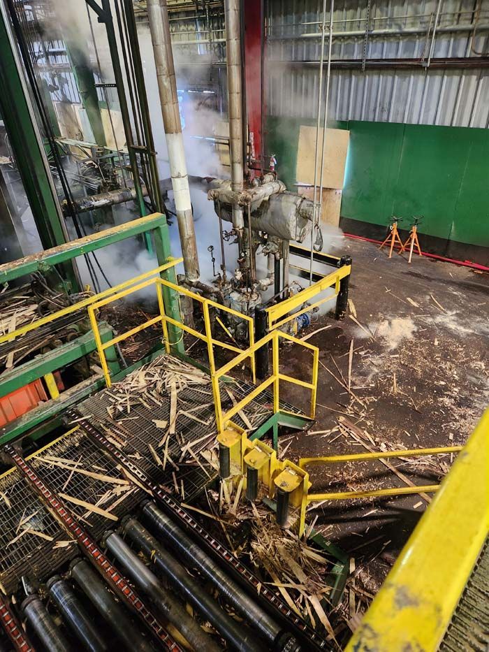 An industrial facility floor with metal railings, wooden debris, and steam rising near large mechanical equipment.