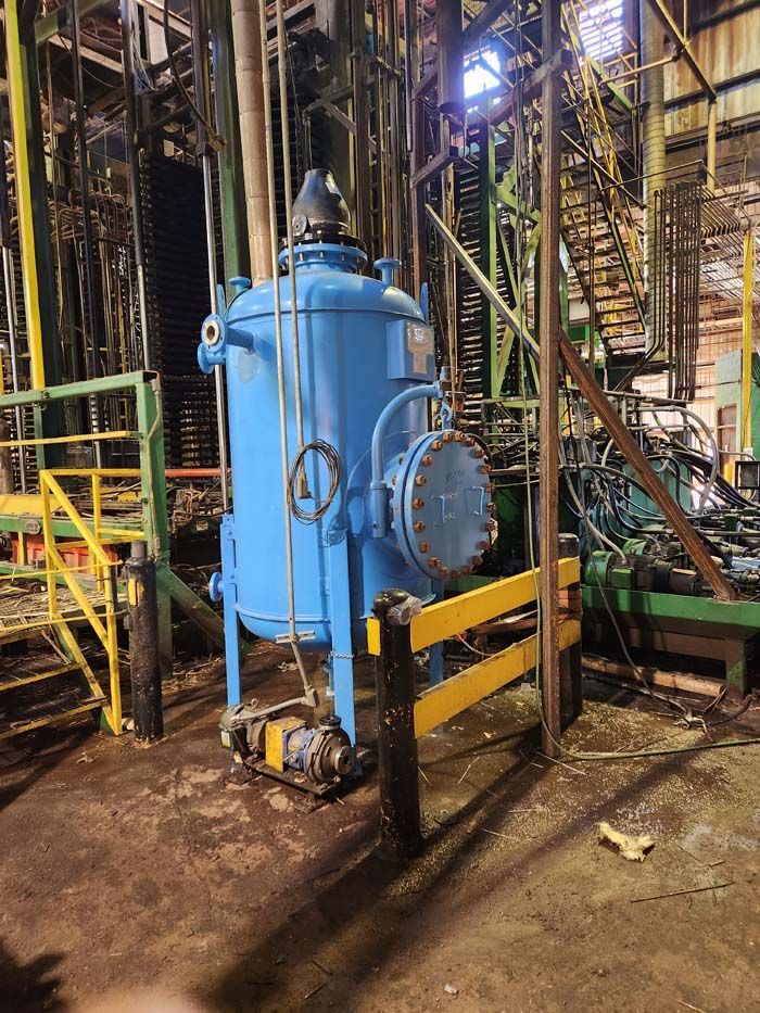 A large blue industrial tank stands in a factory setting, with yellow safety railings nearby and complex machinery behind.