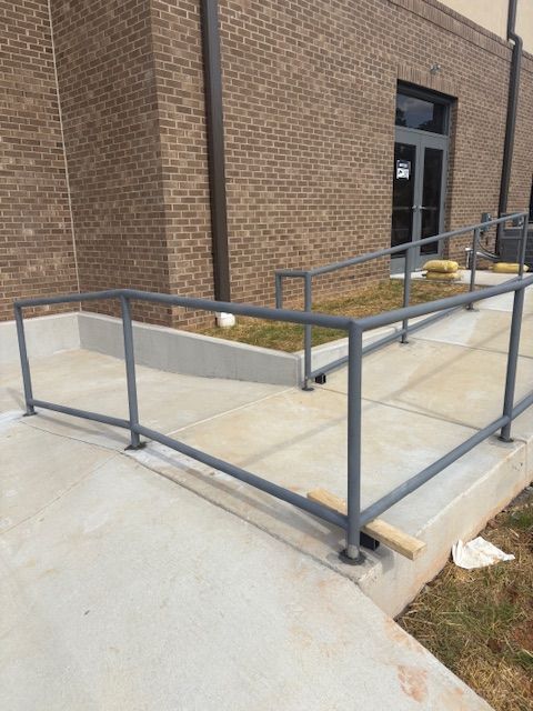 A concrete ADA wheelchair ramp with gray metal handrails leading to a building entrance.