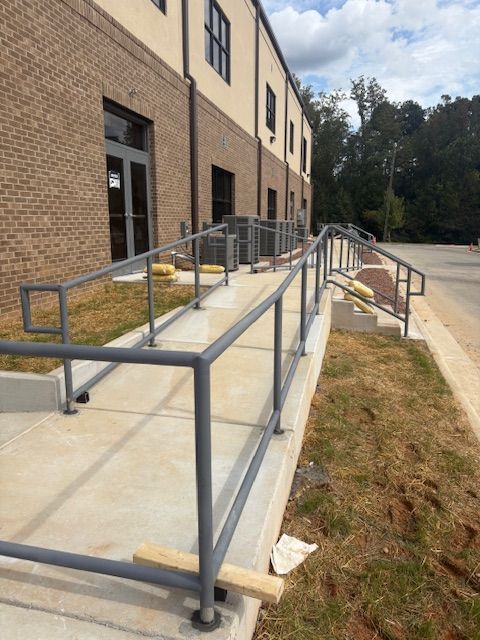 A gray metal ramp with railings runs alongside a brick building leading to an entrance, set against a grassy area.